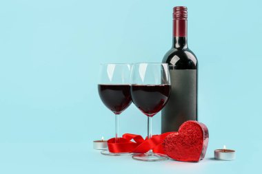 Glasses of wine, bottle, burning candles and heart-shaped gift on blue background. Valentine's Day Celebration