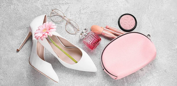 Bag with makeup cosmetics, eyeglasses, female shoes and gerbera flower on grunge background