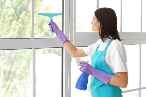 Female janitor cleaning window in office