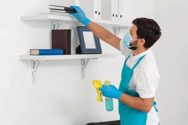Male janitor with medical mask cleaning in office