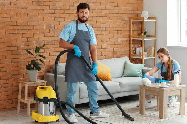 Male janitor hoovering carpet in living room