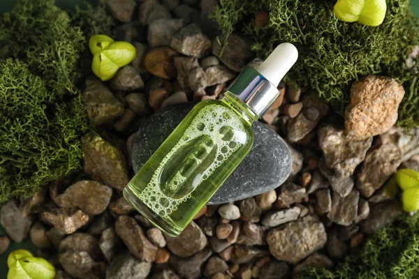 Cosmetic dropper bottle and green moss on rocks, closeup