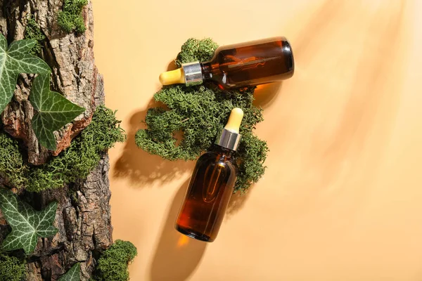 Cosmetic dropper bottles with green moss and tree bark on beige background