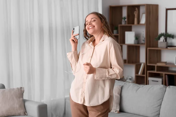 Young woman in earphones with mobile phone dancing at home