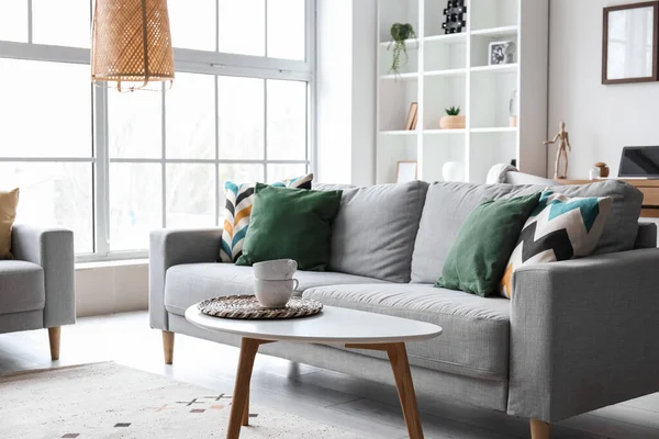Interior of modern living room with grey sofa, table and shelving unit