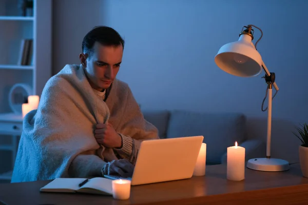 Frozen young man working with laptop in office during blackout