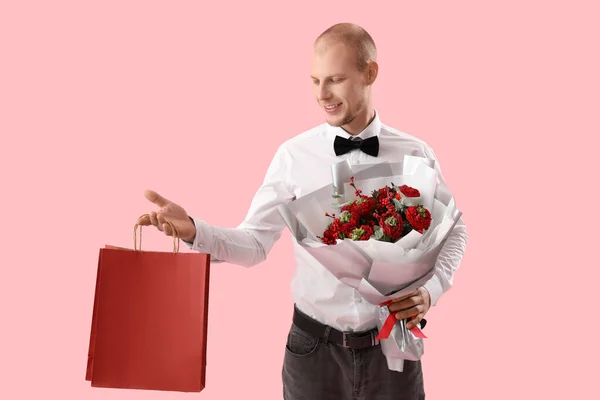 Young man with bouquet of flowers and bag on pink background. Valentine\'s Day celebration