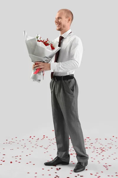 Young man with bouquet of flowers on light background. Valentine's Day celebration