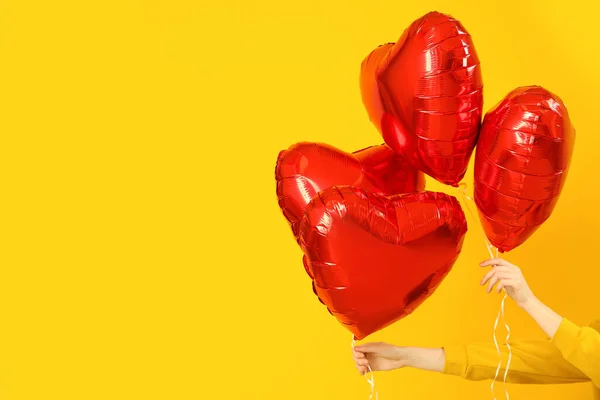 Woman with heart-shaped balloons for Valentine\'s Day on yellow background