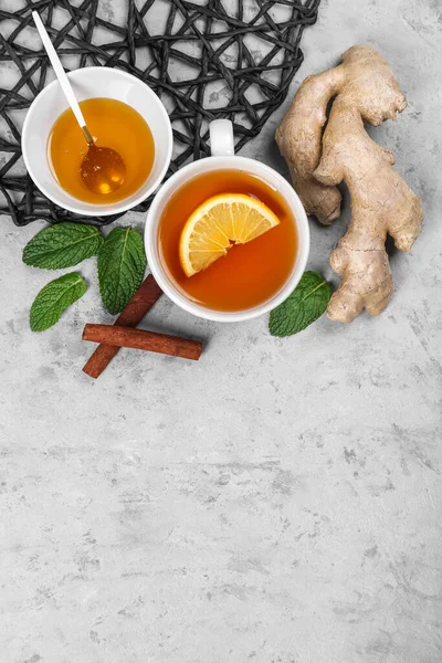 Cup of black tea with lemon, ginger root, honey and mint leaves on grey table