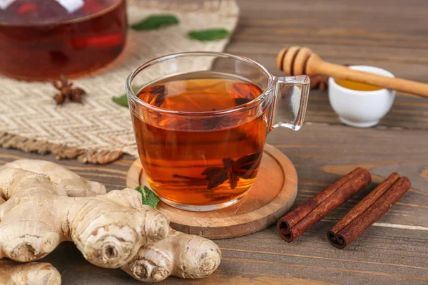Glass cup of black tea, ginger roots, anise and cinnamon on wooden table