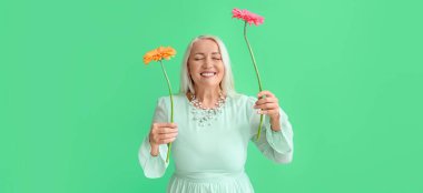 Yeşil arka planda Gerbera çiçekleri tutan gülümseyen olgun bir kadın. Uluslararası Kadınlar Günü kutlamaları