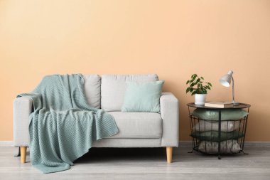 Table with houseplant, lamp, book, cushions and grey sofa near beige wall