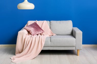 Grey sofa with cushion, plaid and hanging lamp near blue wall