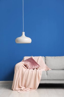 Grey sofa with cushion, plaid and hanging lamp near blue wall