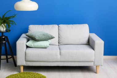 Grey sofa with cushions and hanging lamp near blue wall
