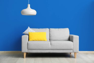 Grey sofa with cushions and hanging lamp near blue wall