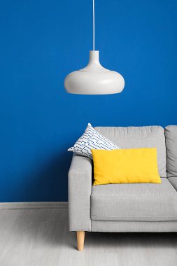 Grey sofa with cushions and hanging lamp near blue wall