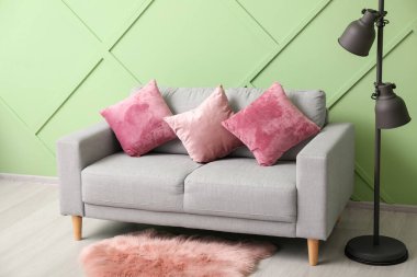 Grey sofa with pink cushions and standard lamp near green wall
