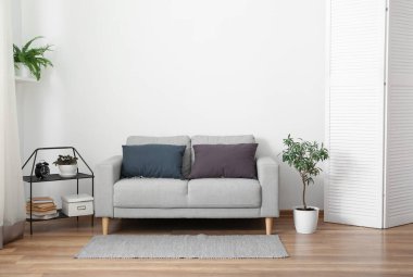 Aydınlık oturma odasının içindeki yastıklı gri kanepe.