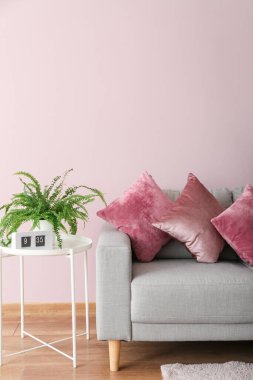 Table with houseplant, clock and grey sofa near pink wall