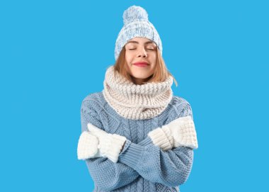 Frozen young woman in winter clothes on blue background