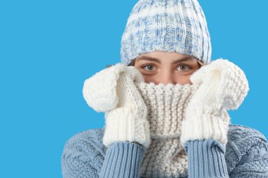 Donmuş genç kadın mavi arka planda kışlık giysiler içinde, yakın plan.