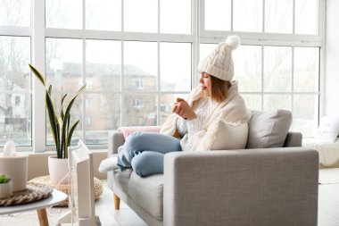 Frozen young woman warming near radiator at home