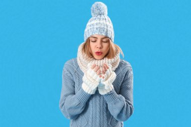 Frozen young woman in winter clothes on blue background
