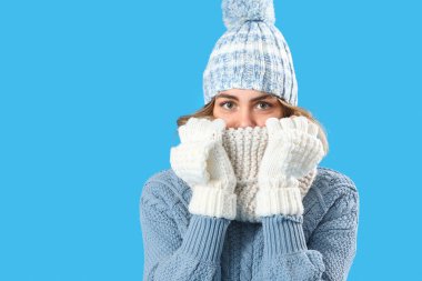 Donmuş genç kadın mavi arka planda kışlık giysiler içinde, yakın plan.