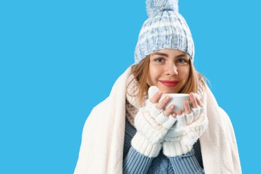 Frozen young woman in warm plaid with cup of coffee on blue background, closeup