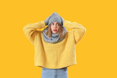 Frozen young woman in winter clothes on yellow background