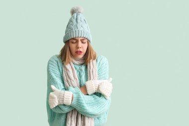 Frozen young woman in winter clothes on green background
