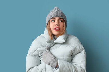 Frozen young woman in winter clothes on blue background