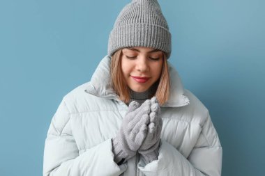 Donmuş genç kadın mavi arka planda kışlık giysiler içinde, yakın plan.
