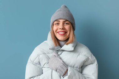 Frozen young woman in winter clothes on blue background