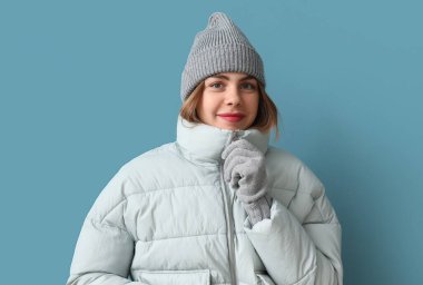 Frozen young woman in winter clothes on blue background