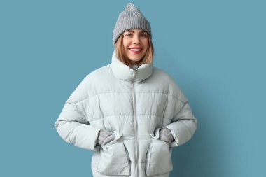 Frozen young woman in winter clothes on blue background
