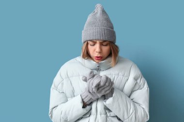 Frozen young woman in winter clothes on blue background