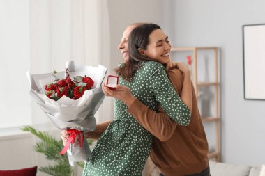 Young man with flowers and ring proposing to his girlfriend at home on Valentine's Day