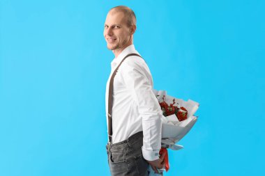 Young man with bouquet of flowers on blue background. Valentine's Day celebration