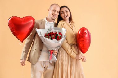 Young couple with bouquet of flowers and balloons on beige background. Valentine's Day celebration