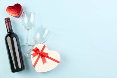Bottle of wine, glasses and heart-shaped gifts on blue background. Valentines Day celebration