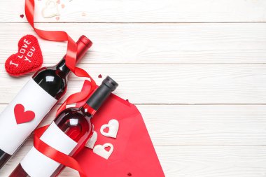 Bottles of wine, heart with text I LOVE YOU, envelope and ribbon on white wooden table. Valentine's Day celebration
