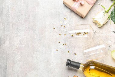 Bottle of wine, gift box, rose flower and glasses on grey table. Valentine's Day celebration