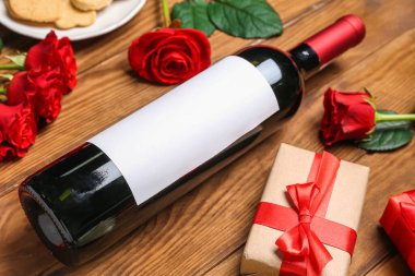 Composition with bottle of wine, rose flowers and gifts on wooden background. Valentine's Day celebration