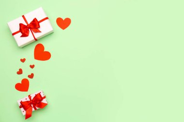 Gift boxes with beautiful bows and paper hearts on green background. Valentine's Day celebration