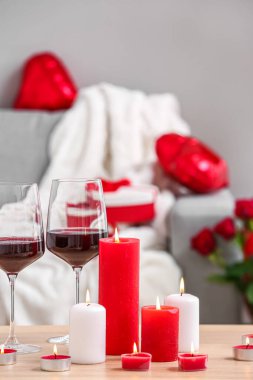 Burning candles and glasses of wine for Valentine's Day on table in living room, closeup