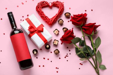 Bottle of wine, chocolate candies, rose flowers and heart on pink background. Valentine's Day celebration