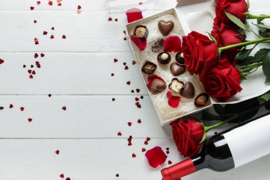 Bottle of wine, box with candies and rose flowers on white wooden background. Valentine's Day celebration